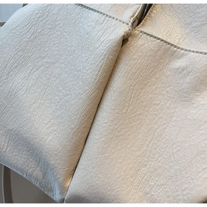 Close-up of cream leather shoulder bag showing fine lychee grain and stitching detail