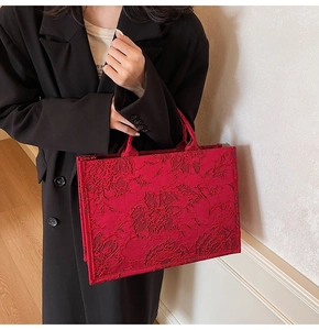 Detail of red floral jacquard tote bag held by a model in a stylish black blazer