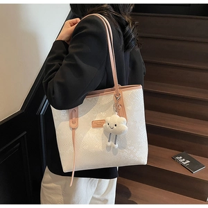 Detail of white snakeskin tote bag with pink handles and cloud plush keychain accessory