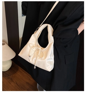 Detail der eleganten Schleife und Metallperlen an einer glänzenden cremefarbenen Tasche