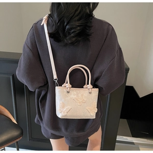 Mini sac seau ivoire avec broderie papillon 3D porté en bandoulière par le mannequin
