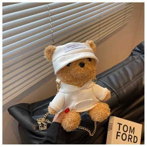 Detail of cute plush bear bag in white hoodie with gold chain strap on a black sofa