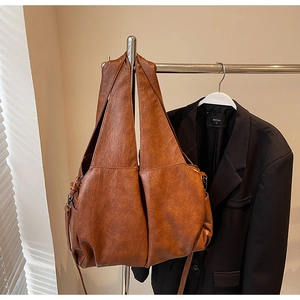 Detail of large brown shoulder bag featuring retro faux leather texture and crescent shape