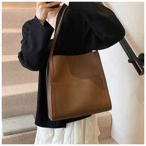 Detail of a large brown tote bag in pebbled leather texture with a front pocket design