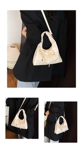 Detail einer cremefarbenen glänzenden PU-Handtasche mit Schleife und Umhängeriemen