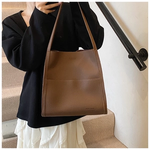 Detailed view of brown litchi grain tote bag with HOCOMU logo worn by a fashion model