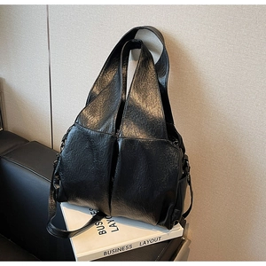 Detail of glossy oil wax leather texture and stitching on a black oversized shoulder bag
