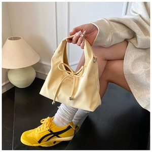 Detail der hellgelben Handtasche mit Schleife und Metallanhänger im 45-Grad-Winkel fotografiert