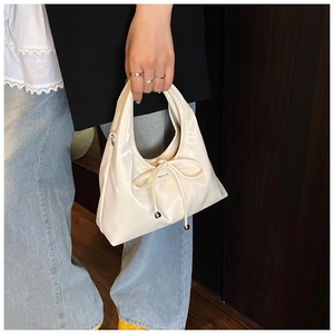 Nahaufnahme der cremefarbenen Schleifenhandtasche mit Glanzleder und Gravur