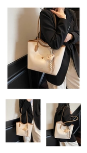 Detail view of large cream tote bag with brown trim, fuzzy bear charm, and striped ribbon