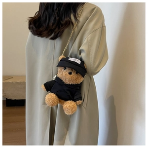 Detail of cute teddy bear plush bag with a black cap and golden chain on a trench coat