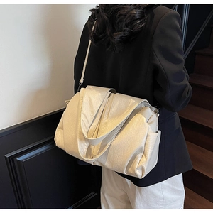 Detail of a large off-white grainy leather tote bag worn by a model in a minimalist setting