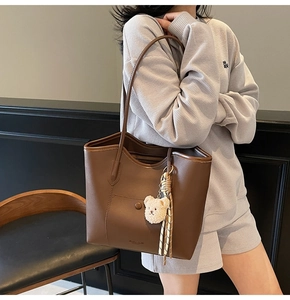 Detail of a brown large-capacity tote bag with bear charm and striped scarf on model