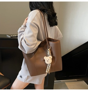 Detail of a large dark brown tote bag with a plush bear charm and sleek leather texture