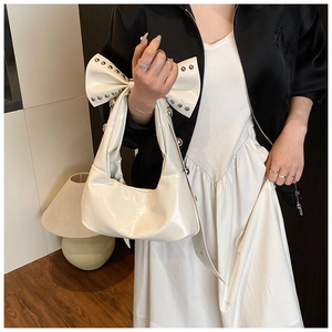 Vue détaillée du sac hobo crème avec grand nœud à rivets et finition en cuir brillant