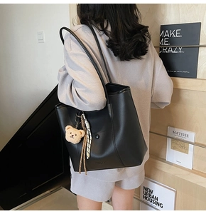 Detail of black matte tote bag with plush bear charm and striped strap shown on shoulder