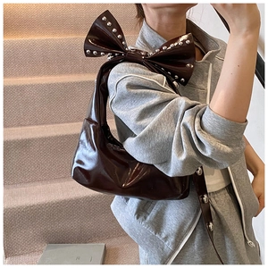 Détail d'un sac à bandoulière en cuir verni marron foncé avec nœud orné de rivets argentés