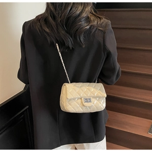 Detail of the elegant quilted chain bag with silver lock on a beige crossbody small purse