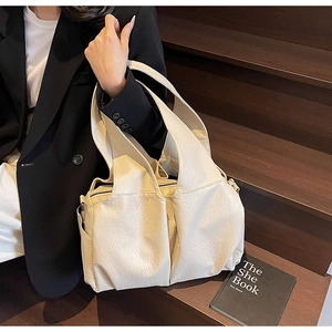 Detail of off-white oversized tote bag with pleated leather texture on dark wood stairs