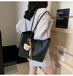 Large black leather tote bag with stitch pocket and white plush bear charm on model
