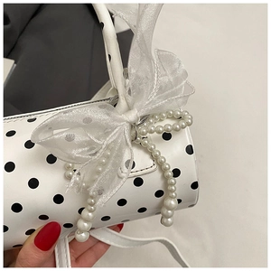 Detailed macro view of polka dot cylindrical handbag with lace bow and pearl chain