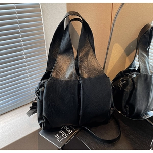 Macro detail of black pleated leather tote bag with wide strap and geometric profile
