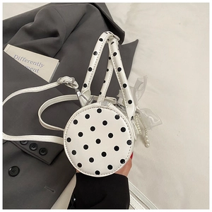 Close-up of a white polka dot cylindrical handbag with bow and pearl chain detail