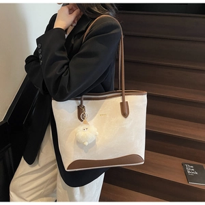 Dettaglio della borsa shopper a contrasto beige e marrone con logo oro e ciondolo peluche
