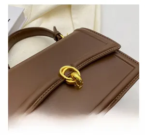 Macro shot of gold metal interlocking buckle and fine stitching on brown leather bag