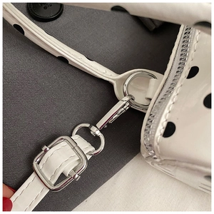 Detailed close-up of adjustable silver hardware and black polka dots on white leather bag