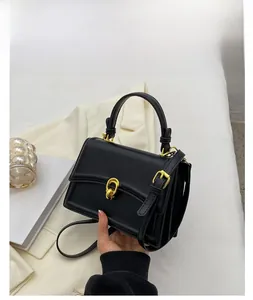 Detail of black leather handbag featuring a secure gold metal lock and adjustable strap