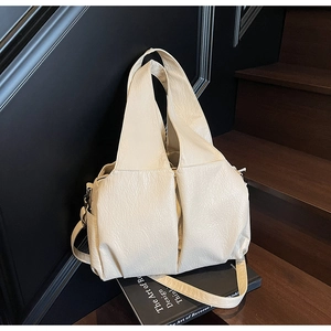 Detail of a large cream-colored shoulder bag with a unique pleated texture on soft leather