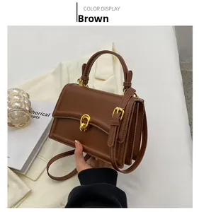 Detail view of brown leather handbag with gold circular clasp on white blazer