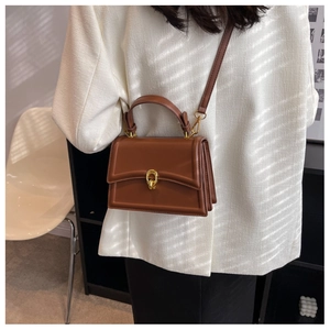 Detail view of a brown vintage square bag with a golden ring buckle on a white textured suit
