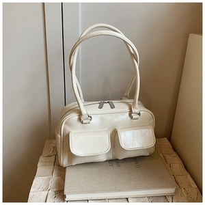 Detail of a creamy beige glossy tote bag with dual front pockets on a stone pedestal