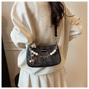 Detail of tweed crossbody bag with pearl chain, metallic heart charm, and fashion label