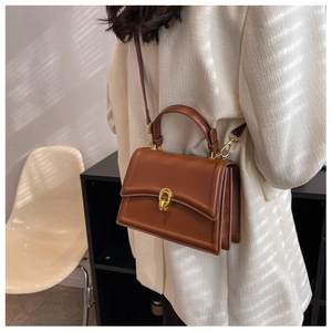 Detail of a brown leather crossbody bag with a gold metal ring lock and top handle