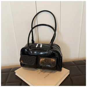 Glossy black underarm tote bag with silver zippers and front pockets on a book