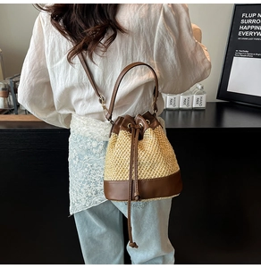 Detail of woven straw bucket bag with dark brown leather trim and drawstring closure