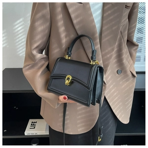 Detailed view of black rectangular handbag featuring a gold U-shaped metal lock and handle