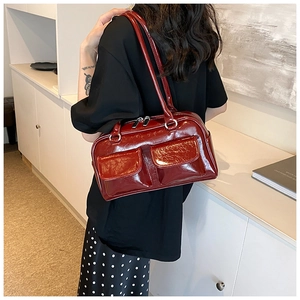 Detail of glossy deep red shoulder bag with metallic zipper pockets worn by a model