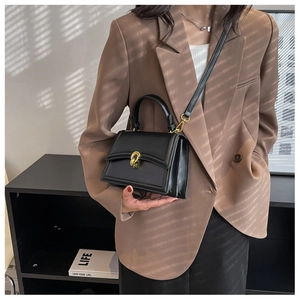 Detail of black leather handbag featuring a golden metal twist lock and accordion side structure