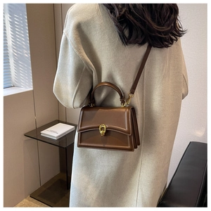 Detail view of brown leather crossbody bag featuring gold ring twist lock and accordion sides