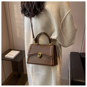 Detailed side view of dark brown leather handbag with vintage gold buckle and accordion sides