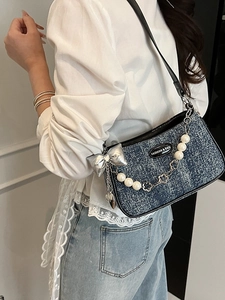 Women denim crossbody bag with pearl chain and bow detail shown on a model