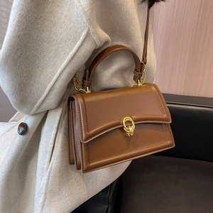 Brown square leather handbag with golden knot buckle worn by model on white coat