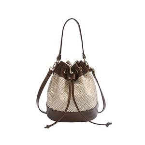 Woven straw bucket bag with dark brown leather trim and drawstring for summer beach vacation