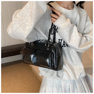 Close-up of black glossy patent leather tote bag with dual front flap pockets and silver zippers