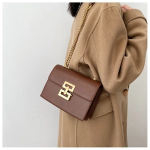 Sac à chaîne en cuir marron avec fermoir doré porté sur un manteau en laine camel