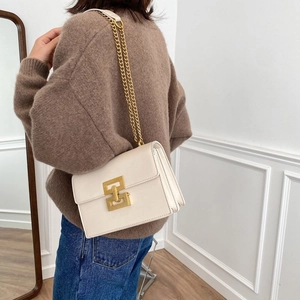 Sac bandoulière blanc avec chaîne dorée et fermoir carré porté à l'épaule par un mannequin